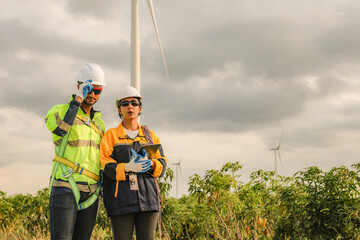 Male and female technical engineers enter the wind farm project area carrying rope pulleys and...
