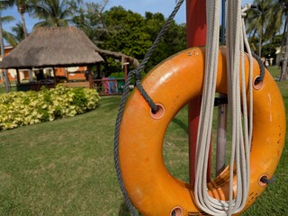 Bright orange life preserver hanging on a red post in a tropical resort garden, surrounded by palm...
