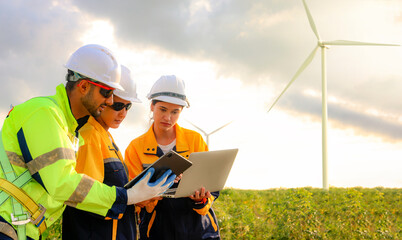 Male and female engineers team walk together wind farm standing tall against cloudy sky sharing...