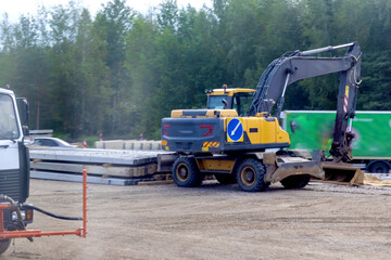 Excavator loading concrete panels at construction site.