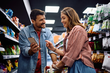 Happy couple using cell phone during a shopping in supermarket.