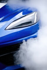 Close up of sleek blue car with angular headlight and smoke billowing around