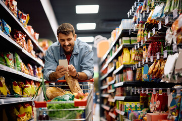 Happy man using smart phone during supermarket shopping.