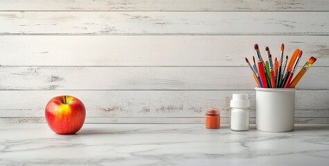 Photo of a white marble countertop with an apple and art supplies on it,