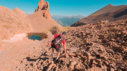 Ascent to the Agujas de Lavasar, in the Pyrenees of Aragon: Mountaineer surrounded by rock formations and large mountains, with the Ibon de Lavasar reflecting the sky and completing the landscape.
