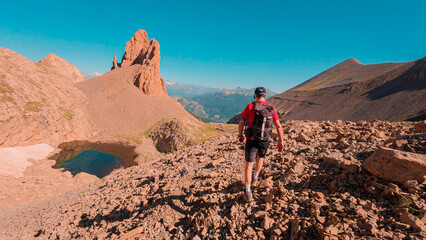 Mountaineer ascending the Agujas de Lavasar in the Aragon Pyrenees, surrounded by large mountains and imposing rocks, with the impressive Ibon de Lavasar at his feet, a unique landscape.
