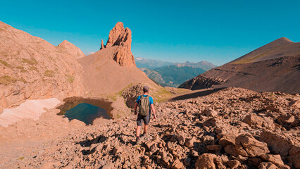 Challenging ascent to the Agujas de Lavasar in the Aragon Pyrenees, a mountaineer overcomes stones and rock formations while enjoying the spectacular views of the Ibon de Lavasar.
