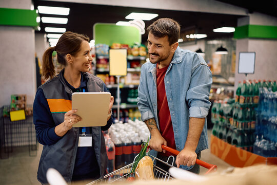 Happy supermarket manager assisting a man in buying groceries at the store. - Powered by Adobe