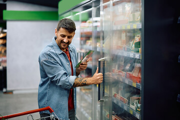Happy supermarket customer taking groceries at refrigerated section.