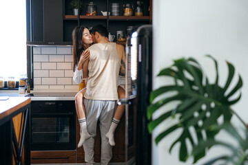 Romantic couple embracing and kissing in a stylish modern kitchen, savoring intimate moments filled with love and joy together