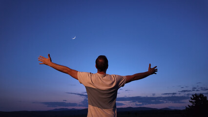 Man with arms wide open enjoying outdoors under stars, planets and Moon.