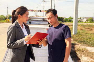 Female officer at a car insurance company service with tow truck stands talking male policyholder...