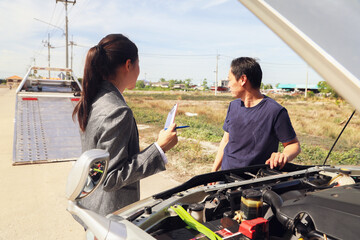 Female officer at a car insurance company service with tow truck stands talking male policyholder...