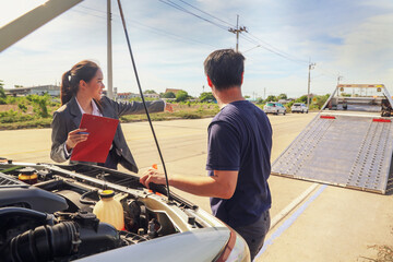 Female officer at a car insurance company service with tow truck stands talking male policyholder...