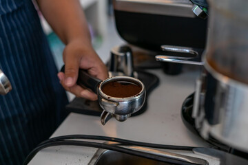 Barista hand holding portafilter with ground coffee, preparing espresso in coffee shop