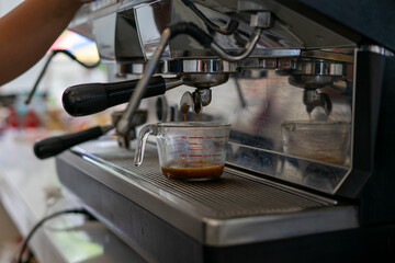 Espresso machine brewing fresh coffee into glass measuring cup, cafe atmosphere, morning energy