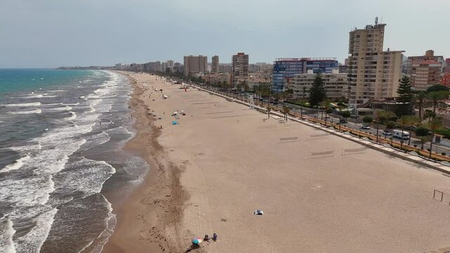 Drone view of Mucha Vista beach stretches alongside a modern cityscape under a clear sky