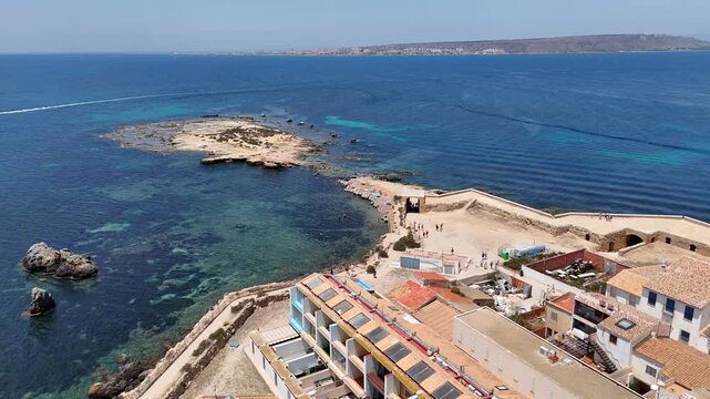 Tabarca Island with coastal buildings along a rocky shore, and vast blue sea under sunny skies