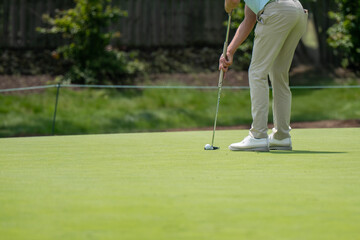 Obraz premium A golfer is captured mid-swing on a pristine green, preparing to putt a golf ball. The image focuses on the action, highlighting concentration in the sport.