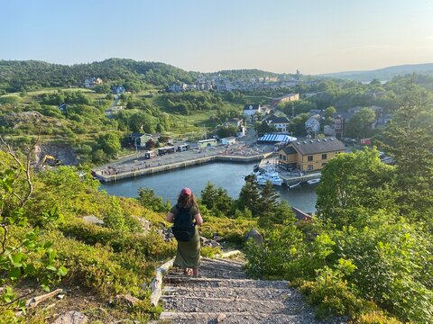 Hiker descends the Sugarloaf Trail, overlooking the scenic fishing village of Quidi Vidi, Newfoundland, with colorful houses and a calm harbor below.