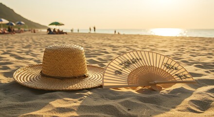 Hat and fan on sandy beach at sunset