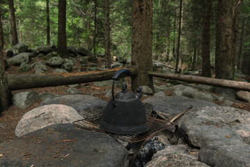 A sooty campfire kettle on a grate in a forest mountain camping in the mountains among pine trees