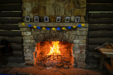 A large stone fireplace with a roaring fire dominates a rustic log cabin interior. Benches flank...