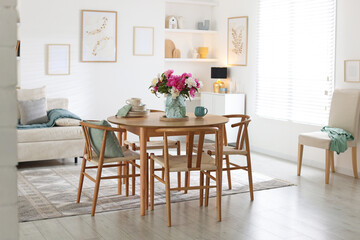 Dining table with beautiful flowers and dishware in room. Interior design