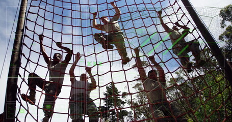 Climbing soldiers in camouflage pants pulling red rope cargo net at forest drill, showing teamwork