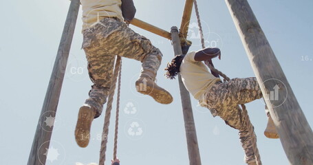 Climbing military partners navigating outdoor obstacle course, with wooden poles and climbing ropes