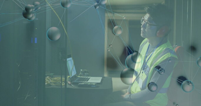 IT tech wearing safety vest, earmuffs monitoring network using laptop at server rack, copy space