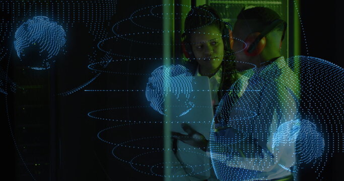 IT technicians wearing ear muffs monitoring server racks on tablet in server room, with data globe - Powered by Adobe