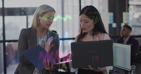 Colleagues reviewing holographic health metrics while holding blue folder and laptop in office