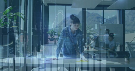 Leaning denim-shirt project manager reviewing documents at office desk, with digital chart graphics