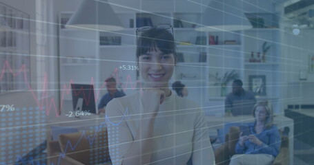 Multiethnic woman analyzing data in open-plan office, with financial charts overlay and monitors
