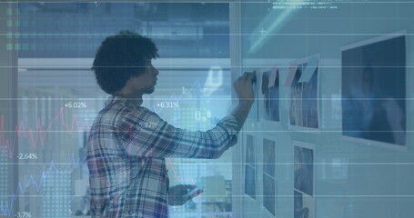 Coordinator in plaid shirt attaching sticky note on office wall, with smartphone and data overlay