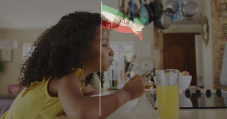 Leaning girl in yellow top using spoon eating from bowl at home countertop, with orange juice