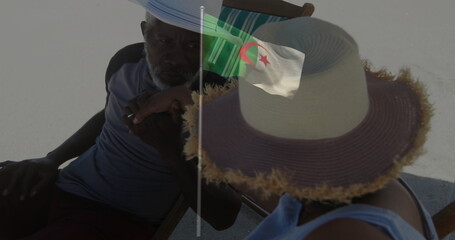 Leaning father and daughter wearing hats holding her wrist on beach chairs, featuring Algerian flag