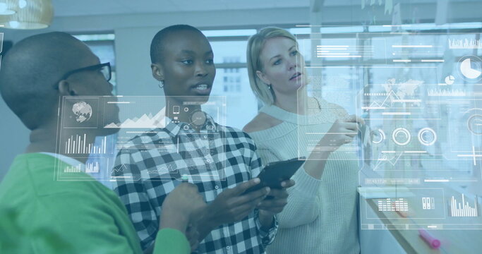 Analyzing co-workers reviewing translucent data projections on glass in modern office, with tablet