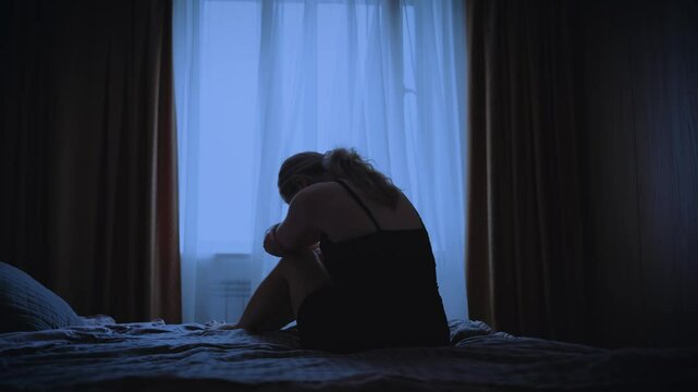 black silhouette upset sunhappy woman sitting on bed dark room, mood depression sadness emotion. Sad lonely Girl feels bad after party, migraine suffers from headache. window curtains white fabric