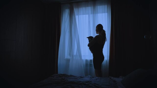 black dark silhouette lonely woman with cat holding pet in hands looking at window, mood depression sadness emotion. Lonely Sad Girl back view. wind blows curtains fly waving white fabric cozy room