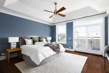 A bedroom with blue walls, white coffered ceiling with a modern fan, cozy bedding and decor, and dark hardwood flooring.