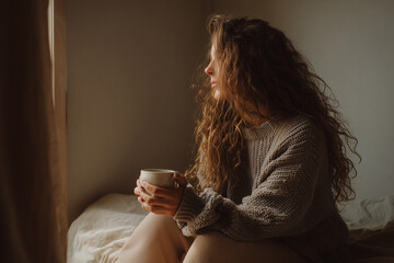 Girl holding tea cup near window in soft light and cozy outfit