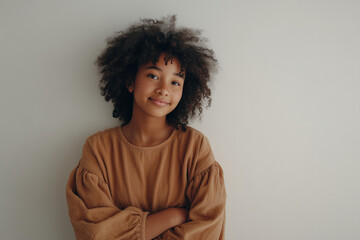 Young Black woman with afro smiling gently against white wall