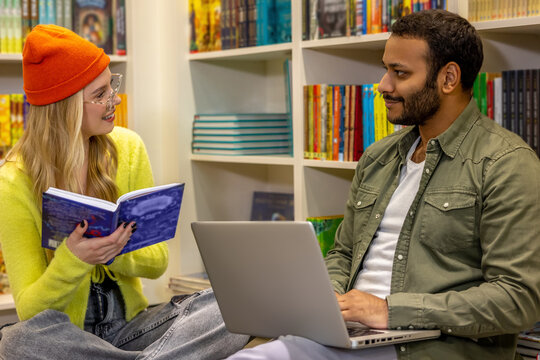 Mixed race couple studying with laptop in library with shelves - Powered by Adobe