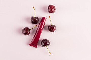 burgundy beauty tube with mask, balm, lip gloss on a pink background among spell cherries. top...