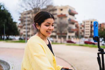 Young woman vlogger recording video blog on phone using tripod in city park