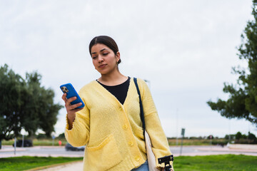 Young woman walking in a park and using her smartphone