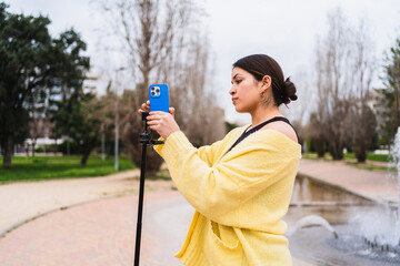 Young woman creating video content for social media using a smartphone on a tripod in a park