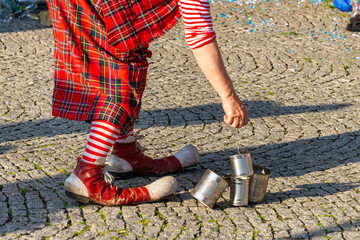 Part of a clown costume during a street performance — red oversized shoes, striped sock, and...